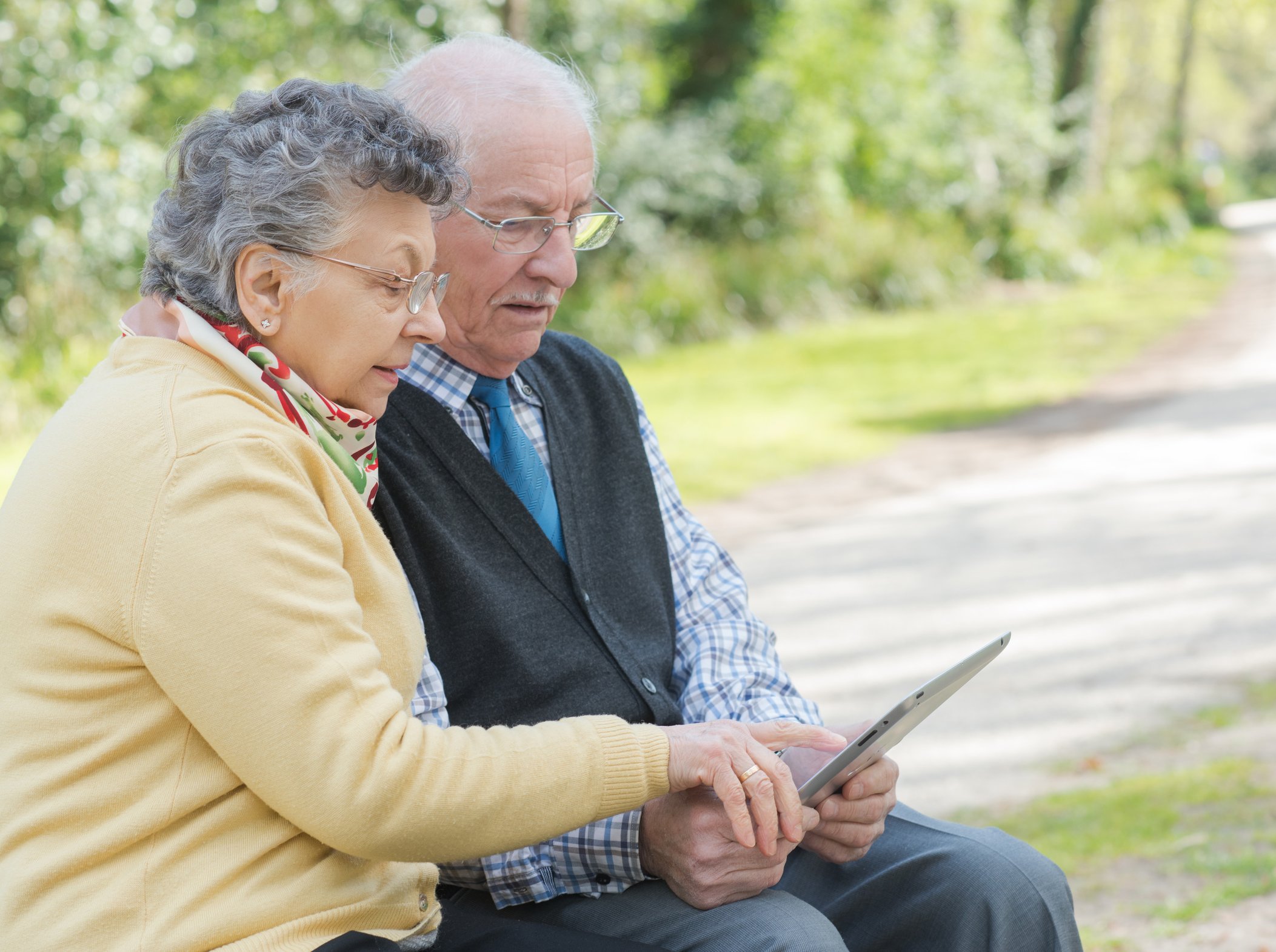 Elderly couple sat on bench looking at tablet